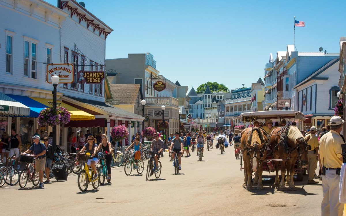 People riding their bikes and walking with also horse-drawn carriage on Main Street of Mackinac Island.