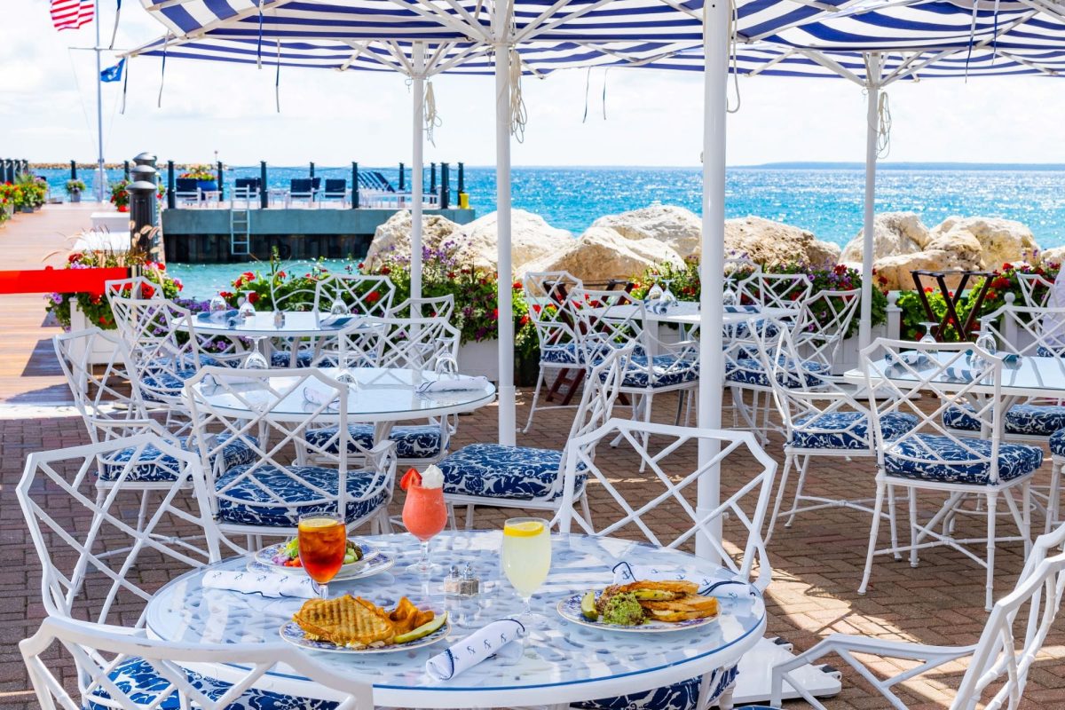 Many tables seated outside with umbrellas with food and drink on them.