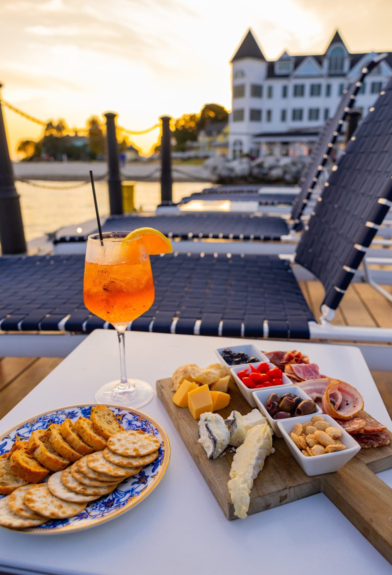 Charcuterie board with cracker and drink on a table with lounging chairs and Hotel Iroquois in the background.