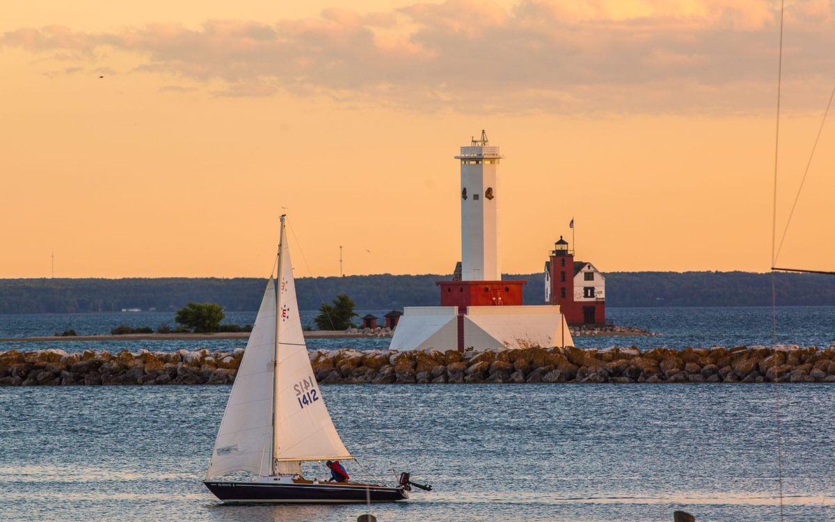 A sailboat in front of a lighthouse.