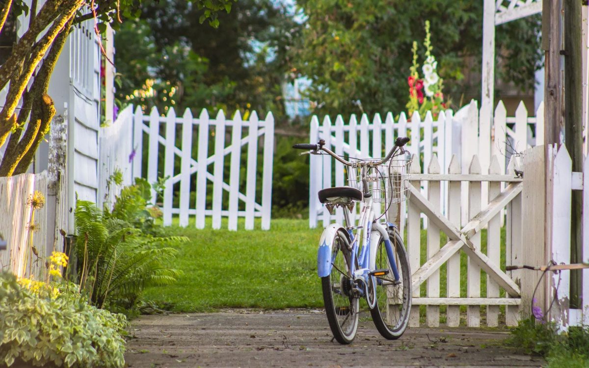 A bicycle in front of a picket fence and green grass.