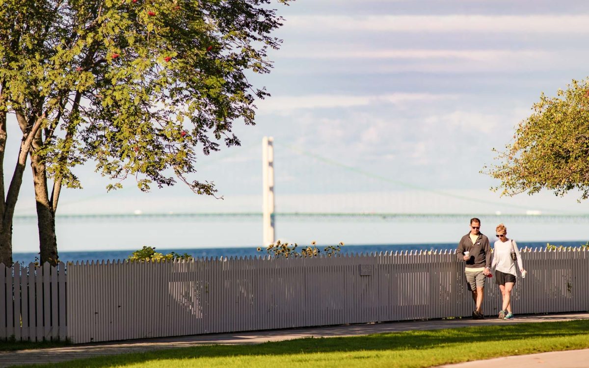 People walking along a walking path with view of the Mackinac Bridge.
