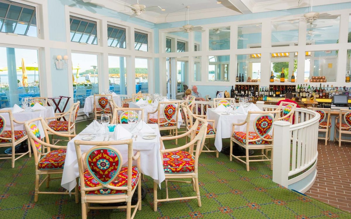 Restaurant dining with many tables and chairs and a blue room with many windows.