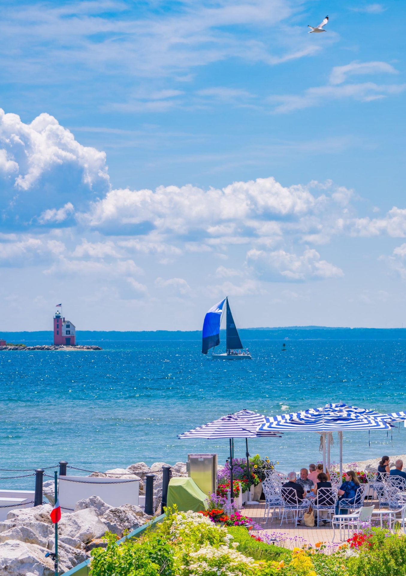 Outdoor dining with people eating looking out onto Lake Michigan with a sailboat and lighthouse