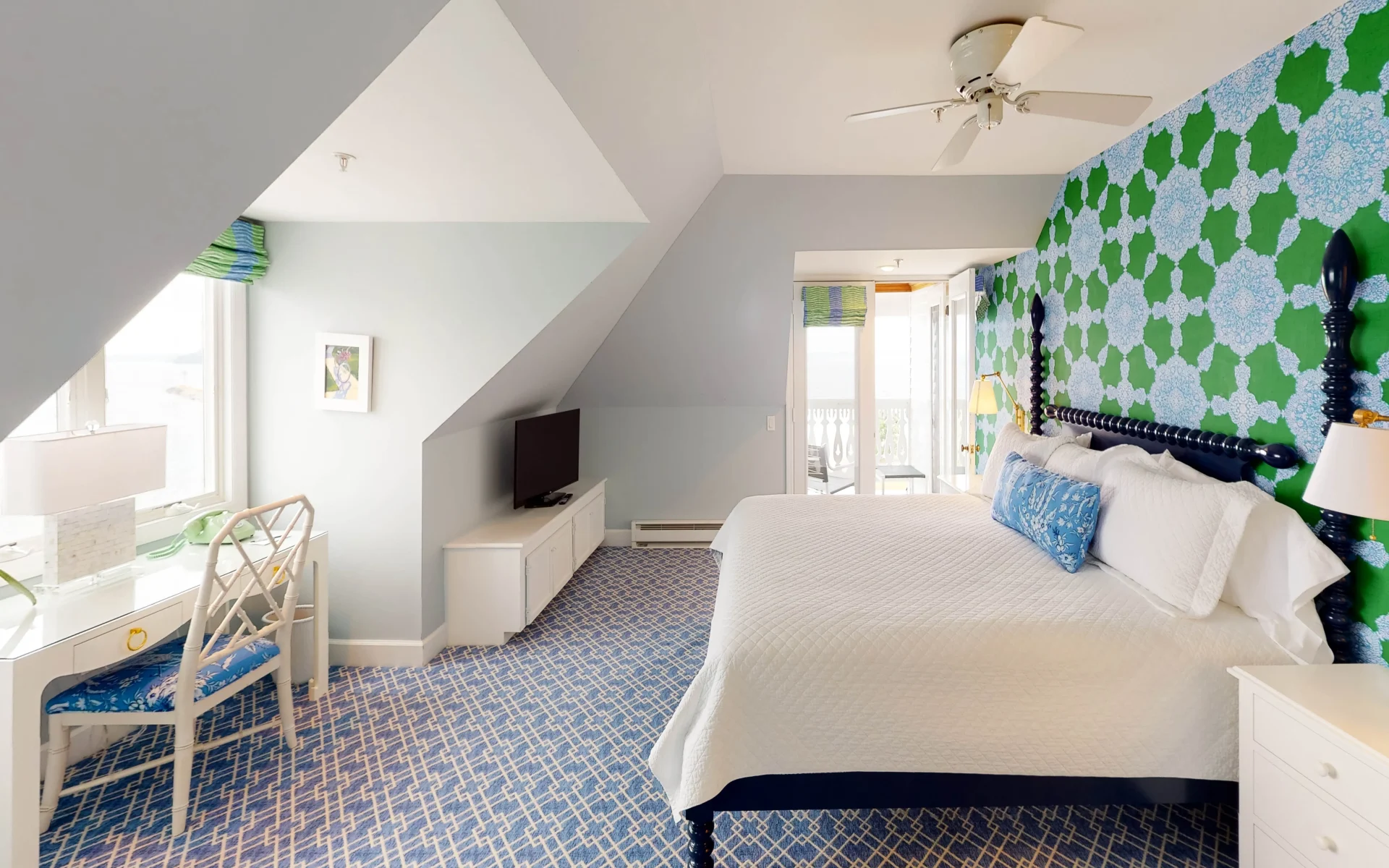 A gray room with green and blue accent wall with blue pattern carpet and white bed with natural light spilling in through windows.