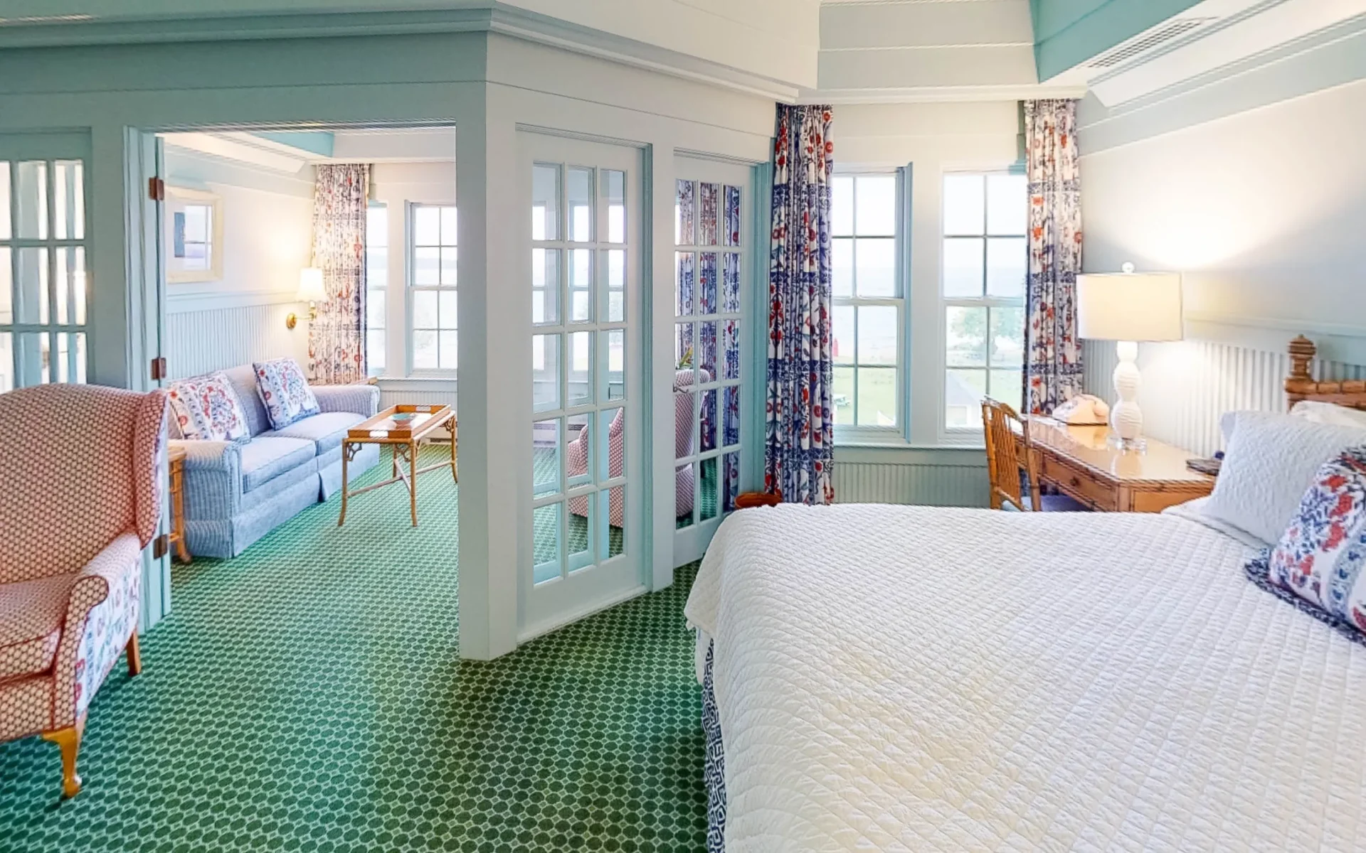 A seating room partitioned off from the bedroom with lots of natural light and windows in a green checkered carpeted room.