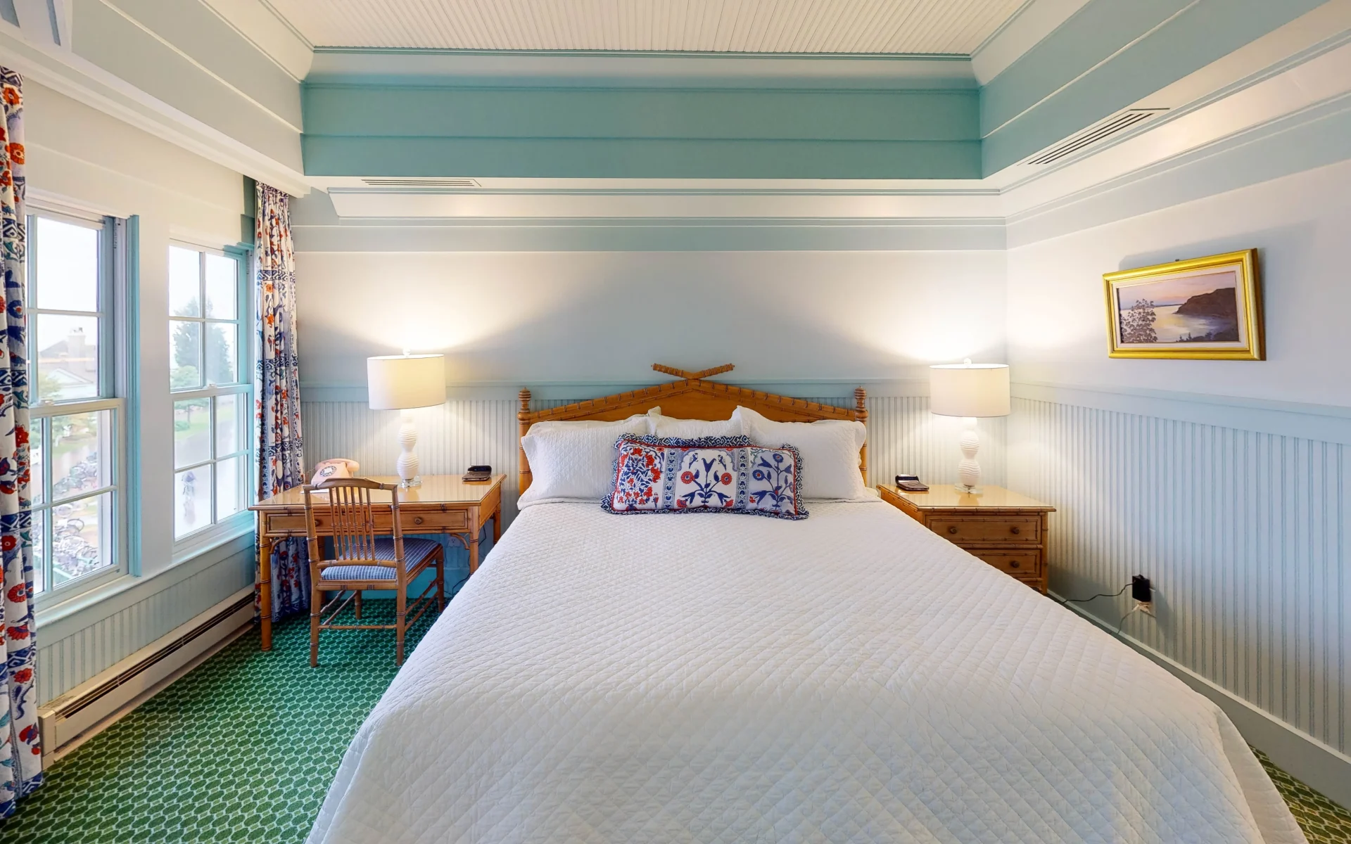 A white bed in a wooden frame in a green and white bedroom with green checkered carpet.