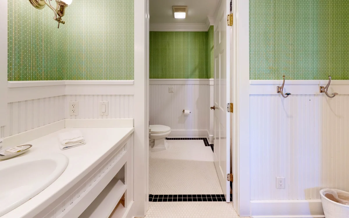 A green and white bathroom with white tile with view of the toilet and sink.