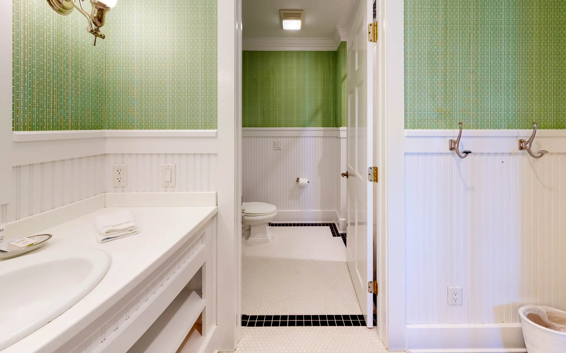 A green and white bathroom with white tile with view of the toilet and sink.