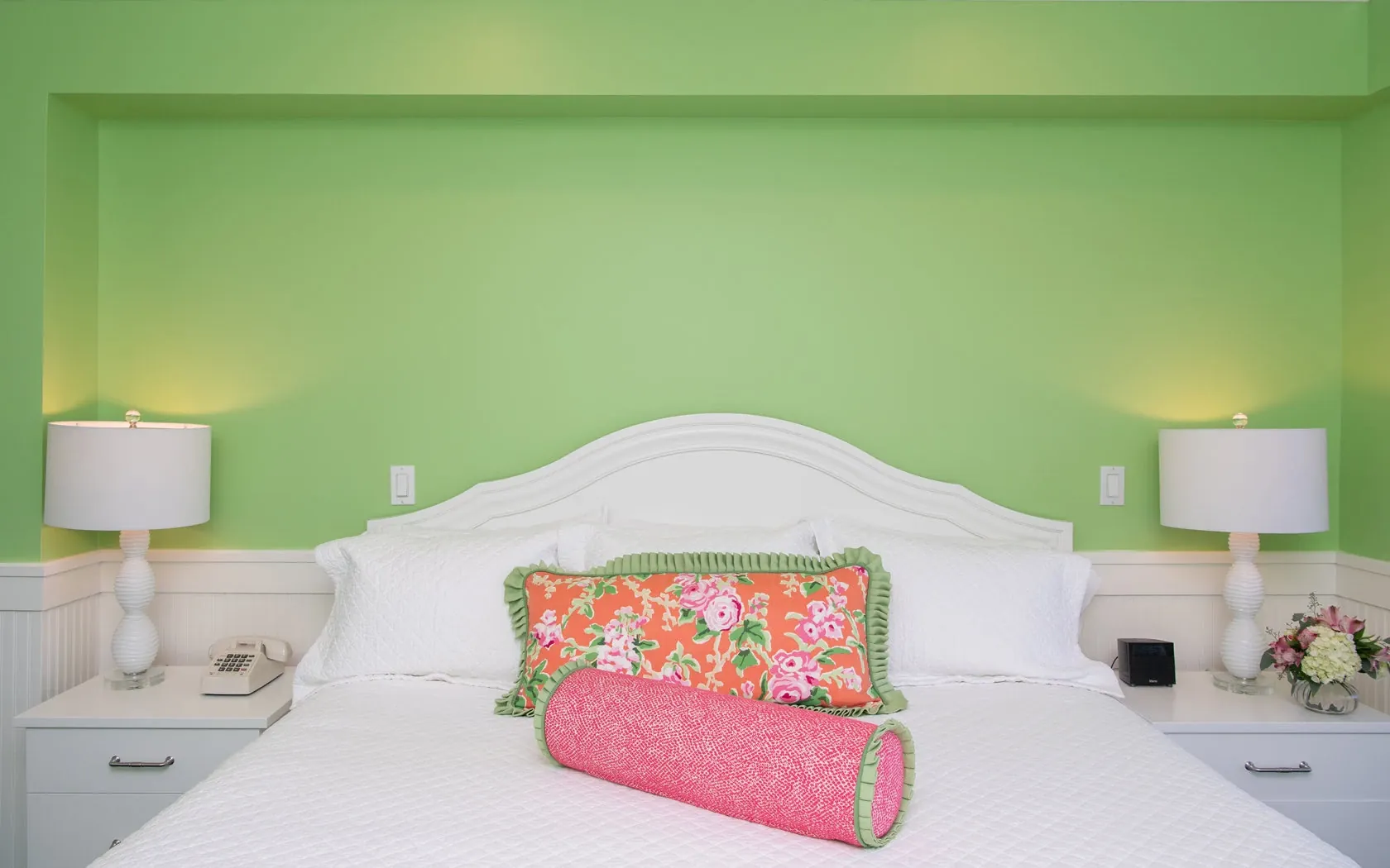 A white bed in a green room with accent pink pillows.