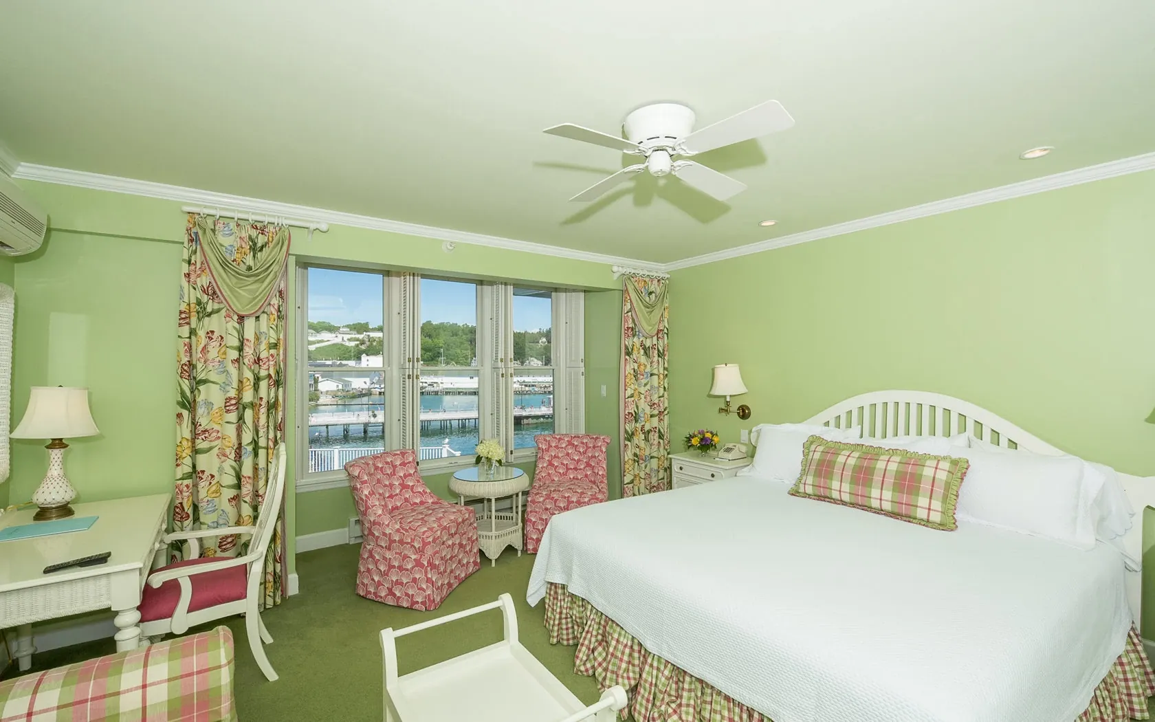 A green room with green carpet with pink chairs and white bed.