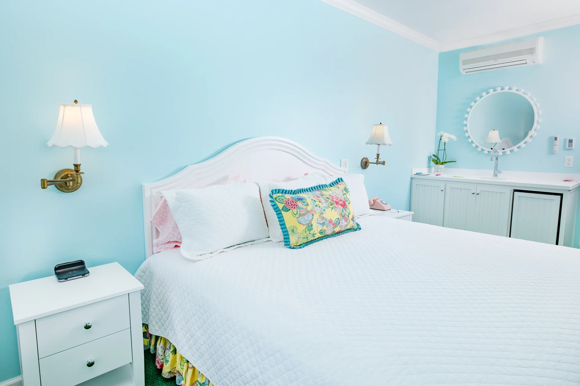 A white bed in a blue painted room with lamps and bedside table.