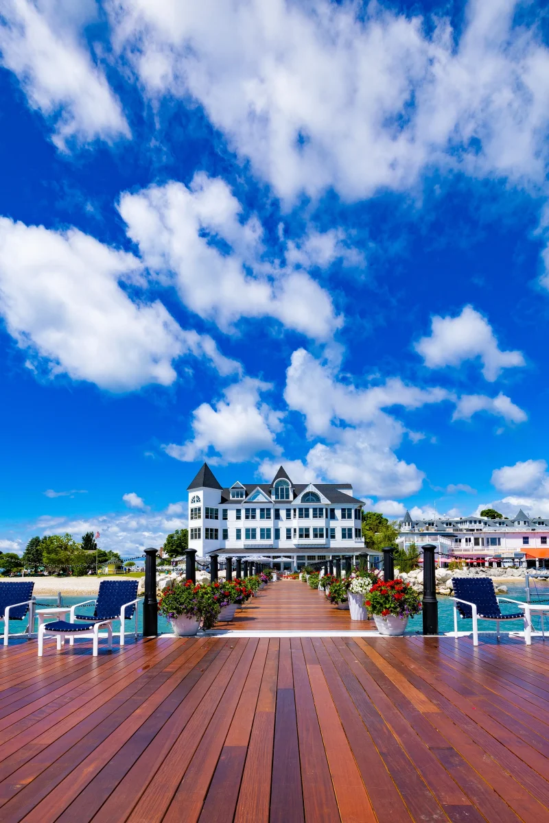 A far-out view of Hotel Iroquois from a wooden dock with clouds in a blue sky.