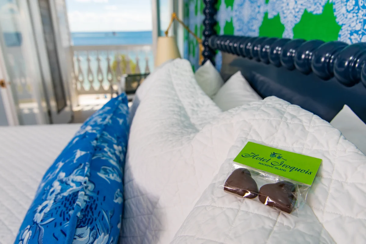 A bed with candies on the top of it and a hotel room with window looking out onto a lake.