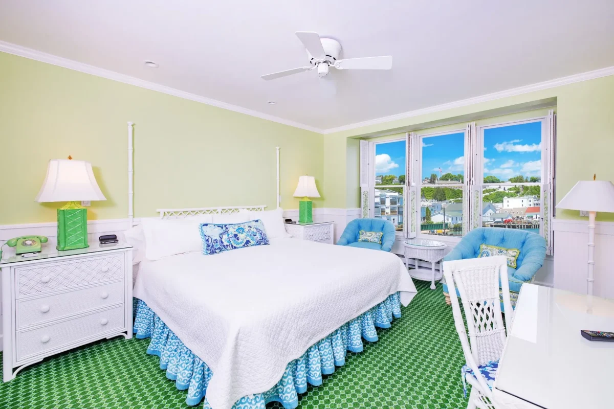 A white bed and a green room with green carpet with ceiling fan and windows.
