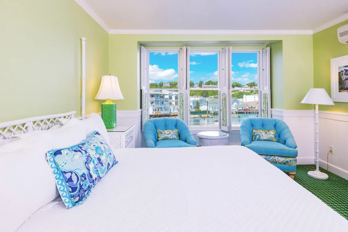 A white bed and a green room with a lamp, windows, and chairs