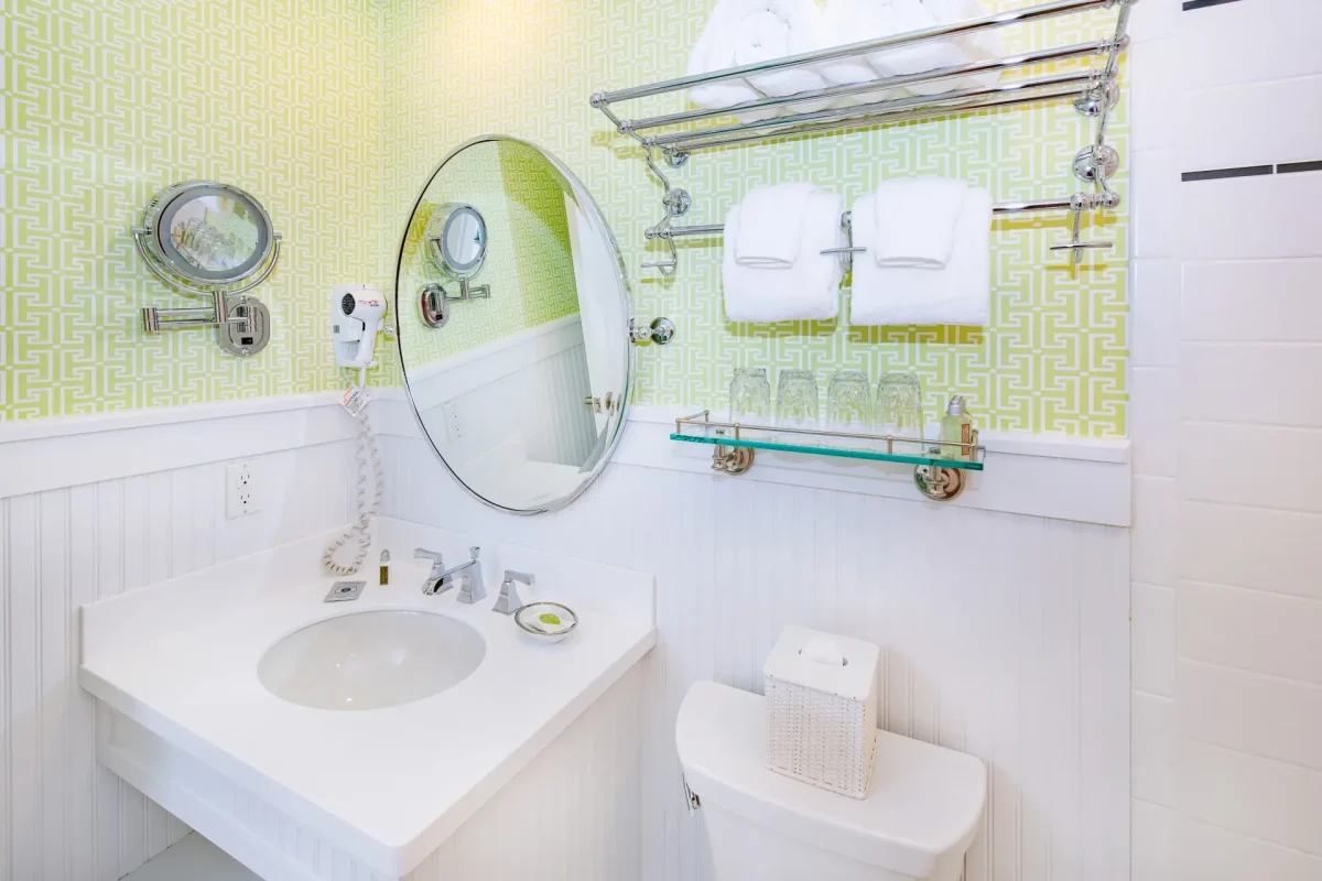 A white bathroom with green wallpaper looking at the toilet sink and mirror.
