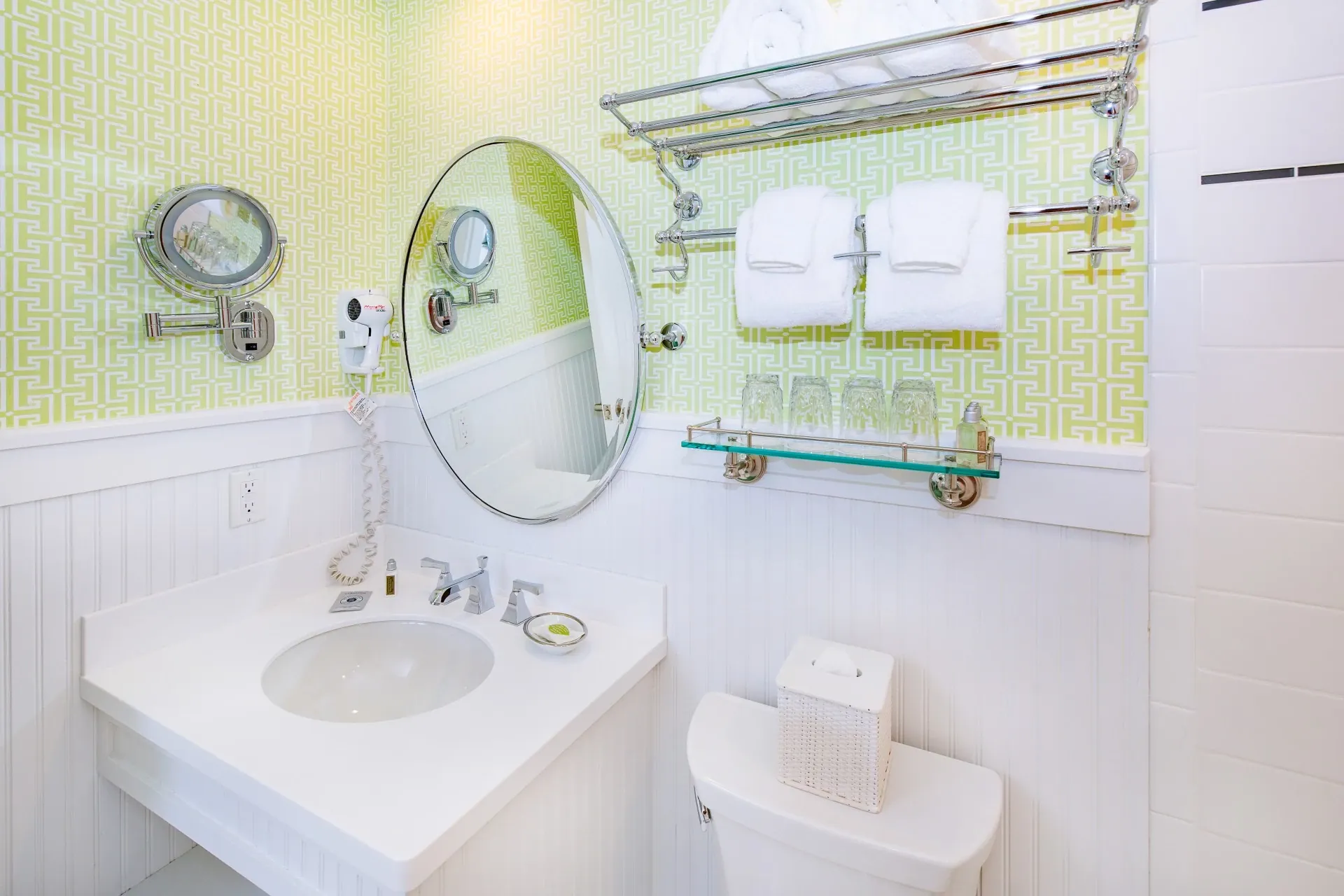 A white bathroom with green wallpaper looking at the toilet sink and mirror.