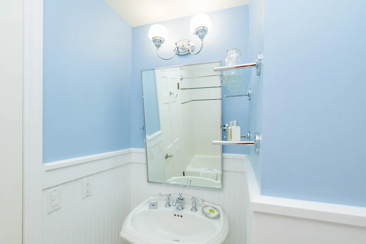 A white bathroom with blue accent color with view of sink, mirror and light.