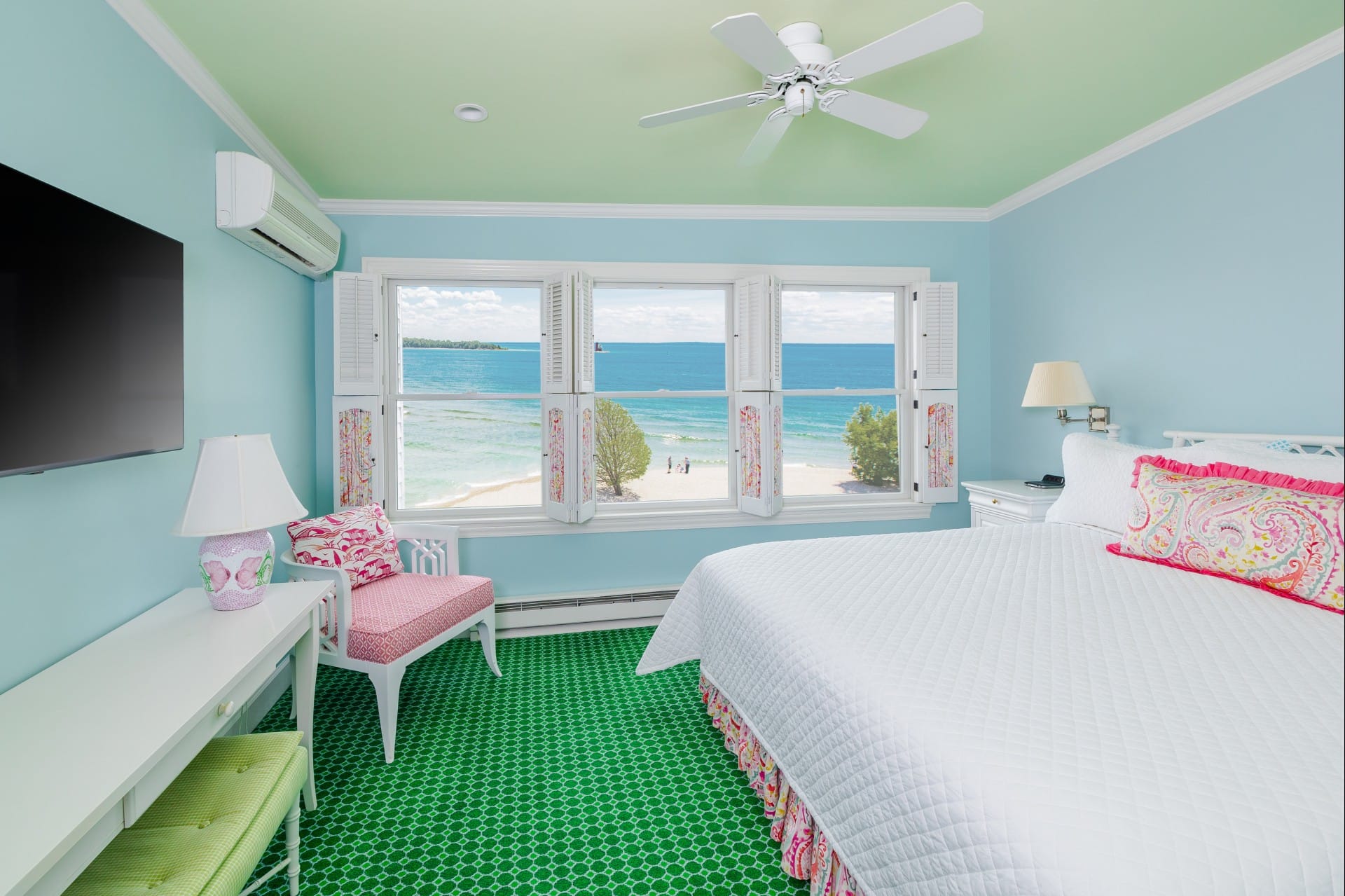 A blue painted room with green carpet, white bed, windows on the wall.