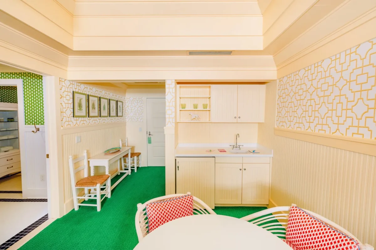 A cream colored room with green carpet and kitchenette.