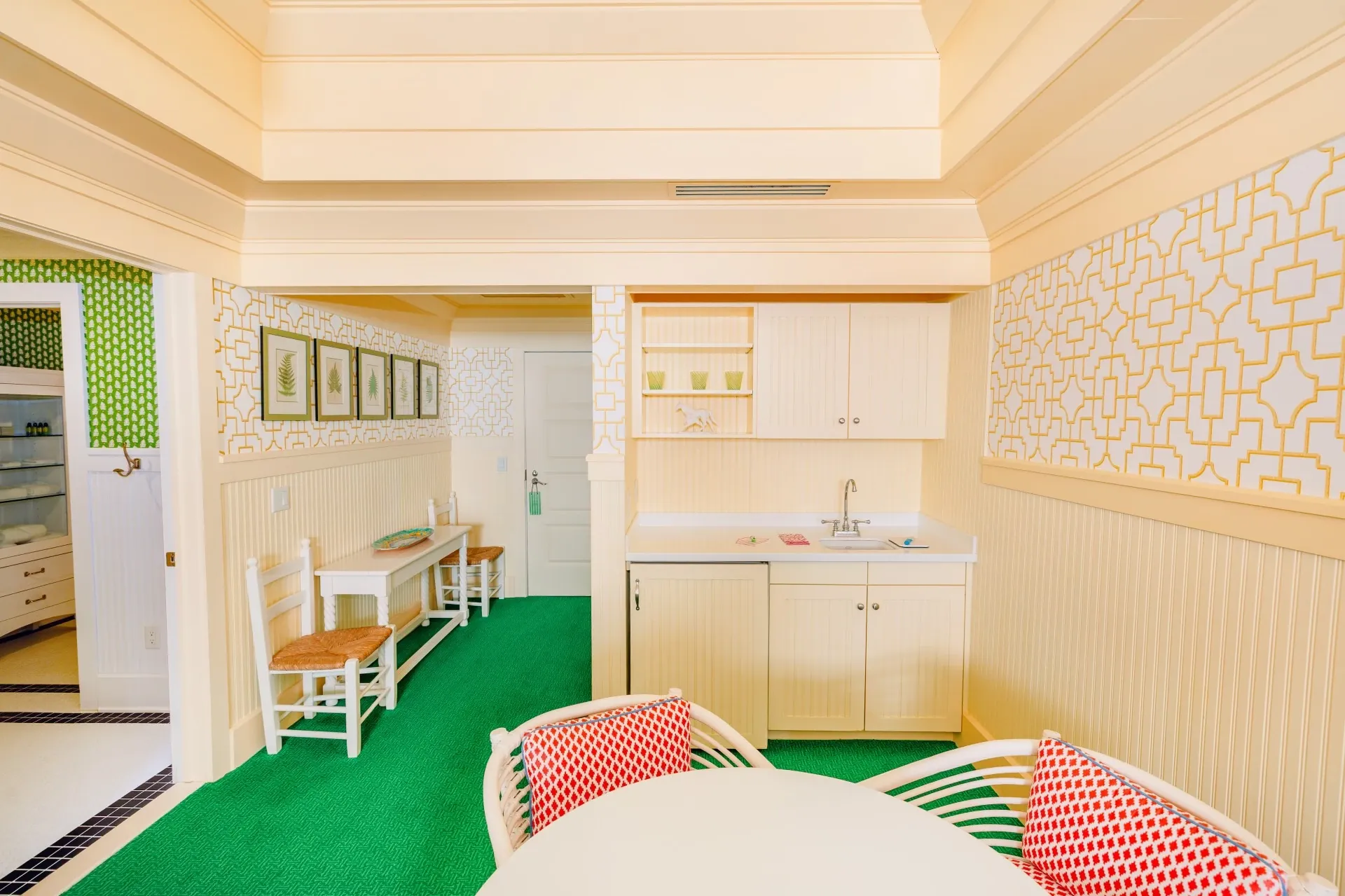 A cream colored room with green carpet and kitchenette.