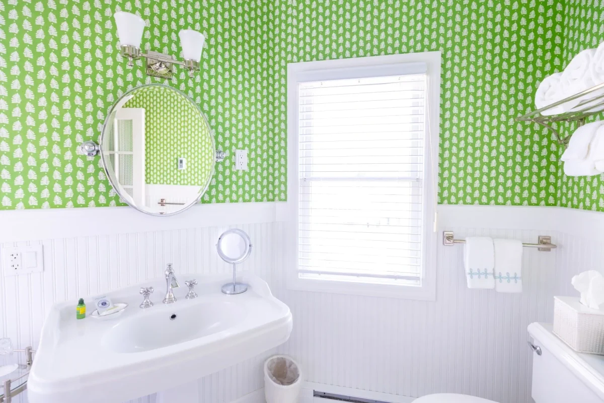 A white bathroom with green wallpaper with view of sink and mirror.