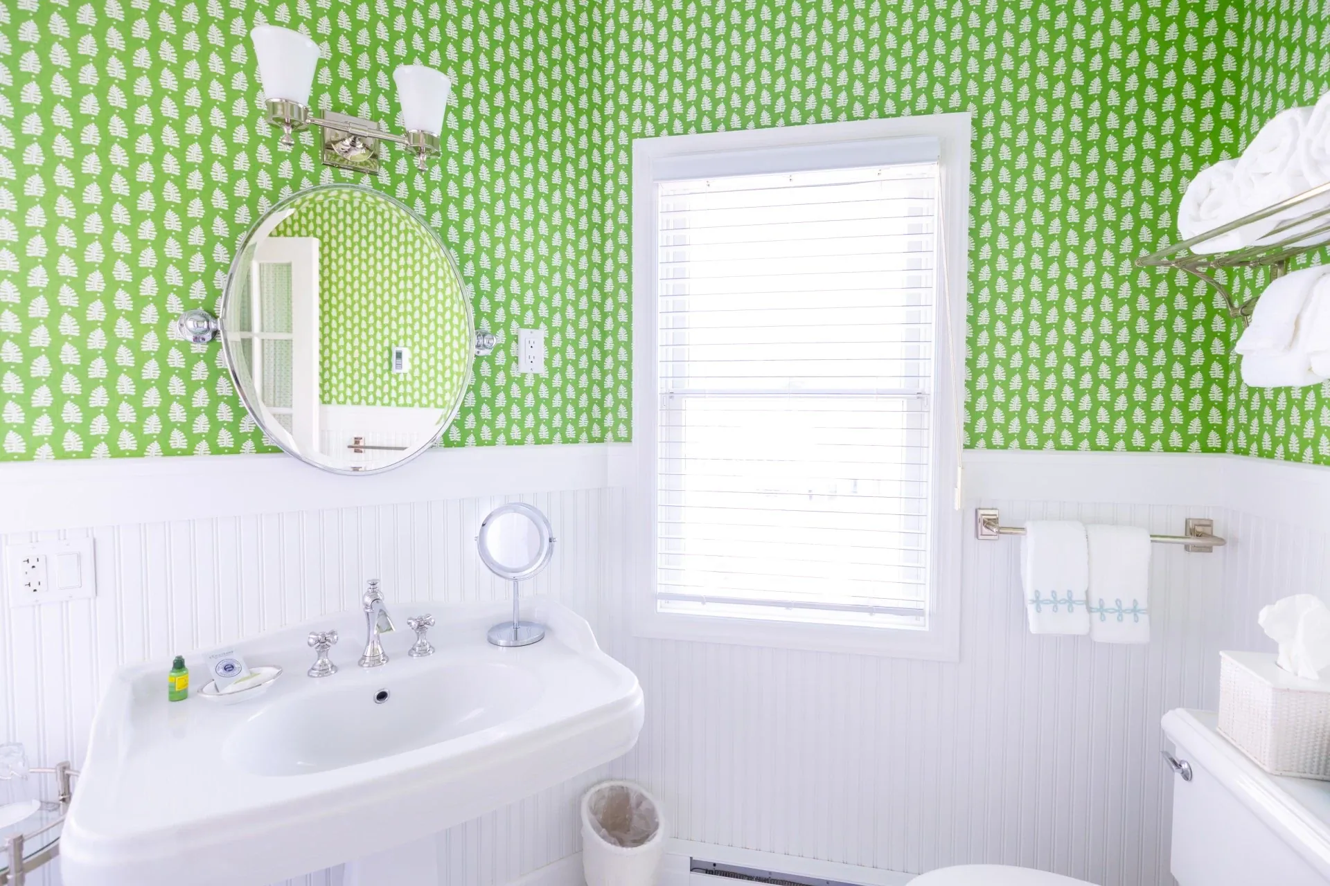 A white bathroom with green wallpaper with view of sink and mirror.