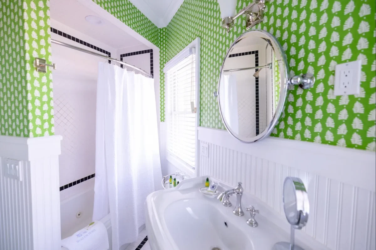 A white bathroom with green wallpaper with view of sink, mirror, and shower.
