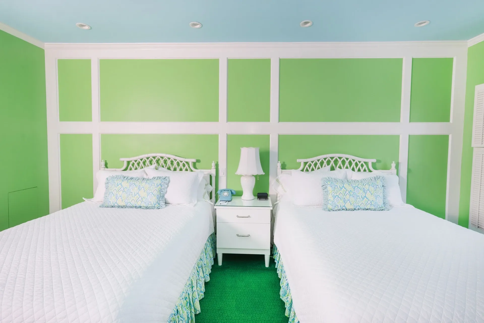 Two white beds in a green room with green carpet and blue ceiling.