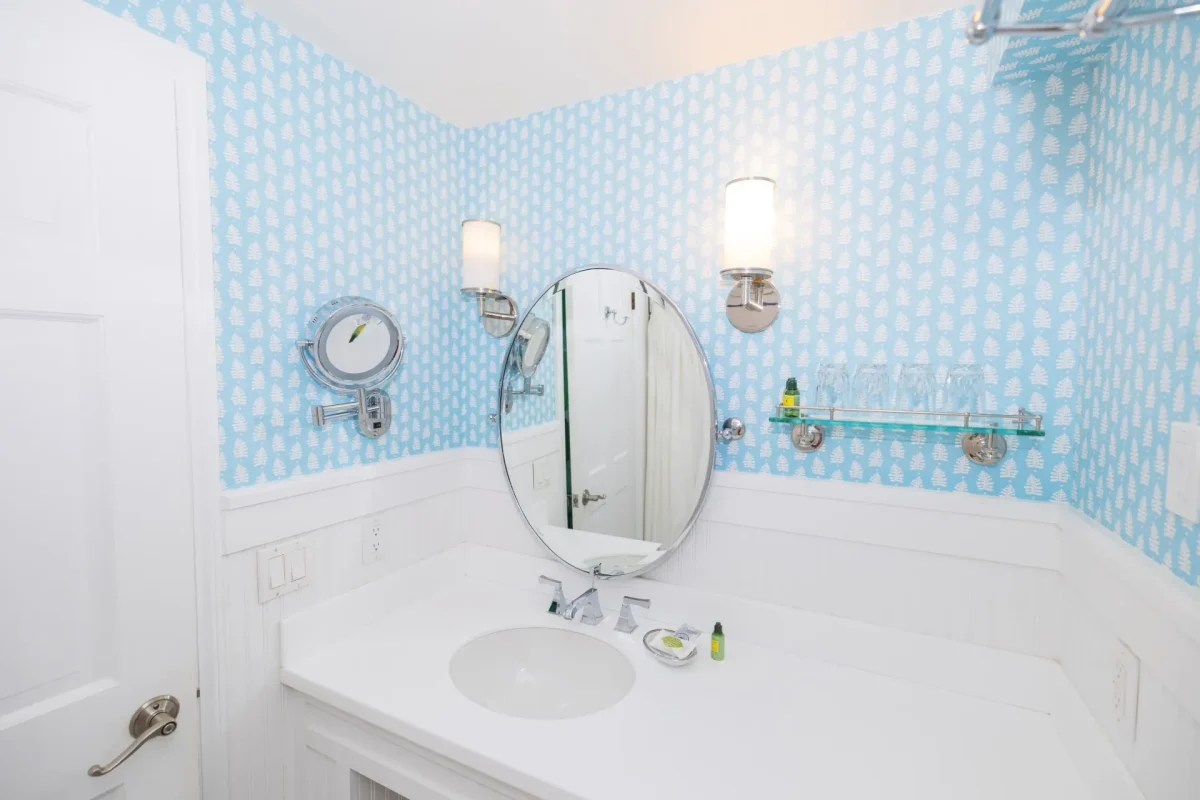 A white bathroom with blue accent wallpaper looking on the sink and mirror.