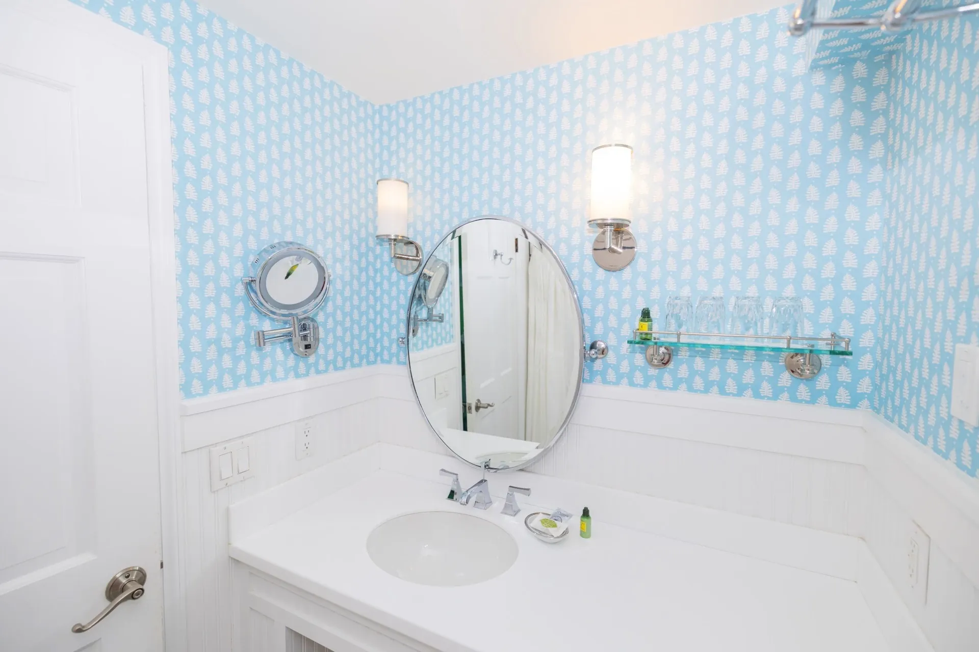 A white bathroom with blue accent wallpaper looking on the sink and mirror.
