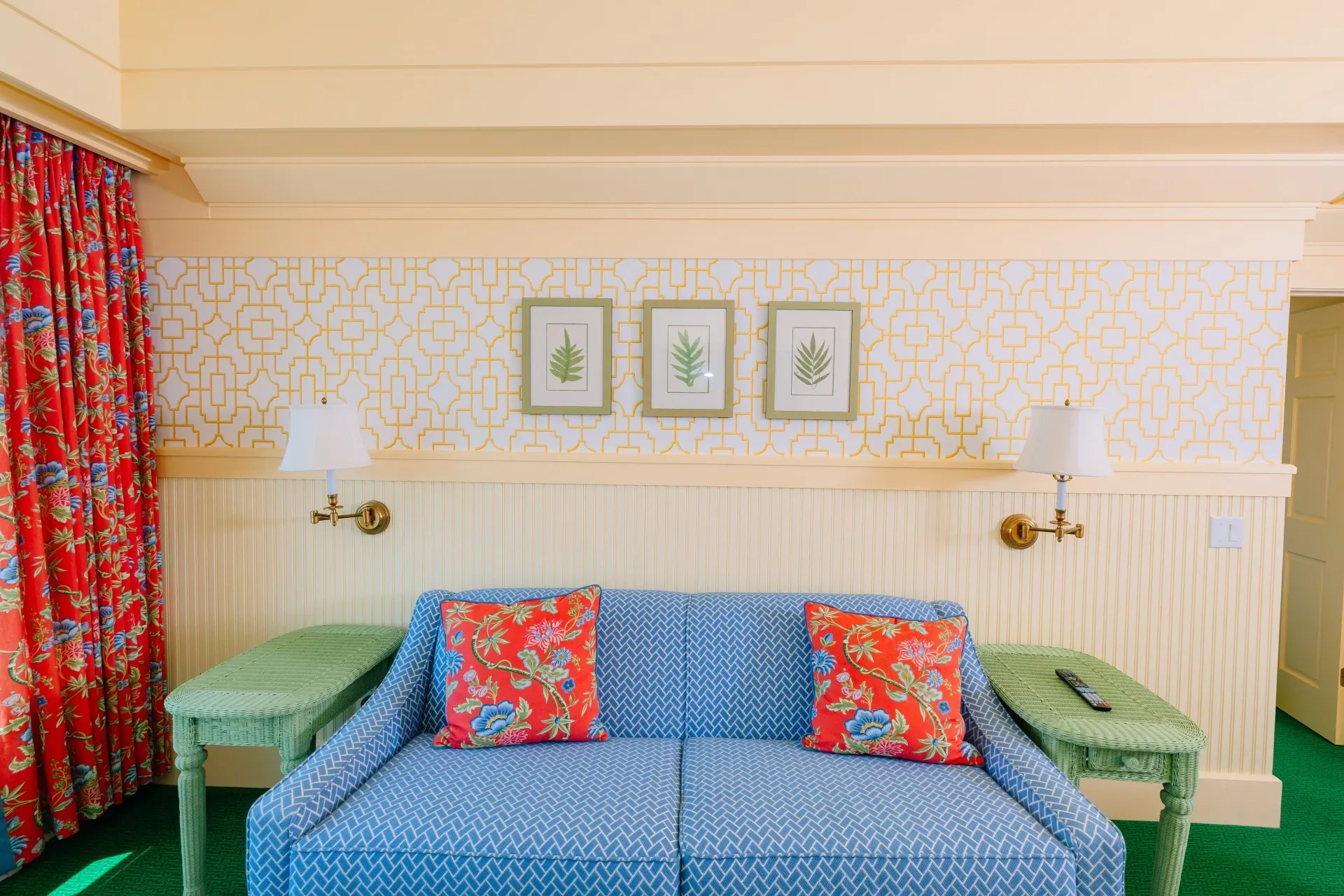 A cream colored room with red curtains, with green carpet, blue couch that has windows looking out onto a lake.