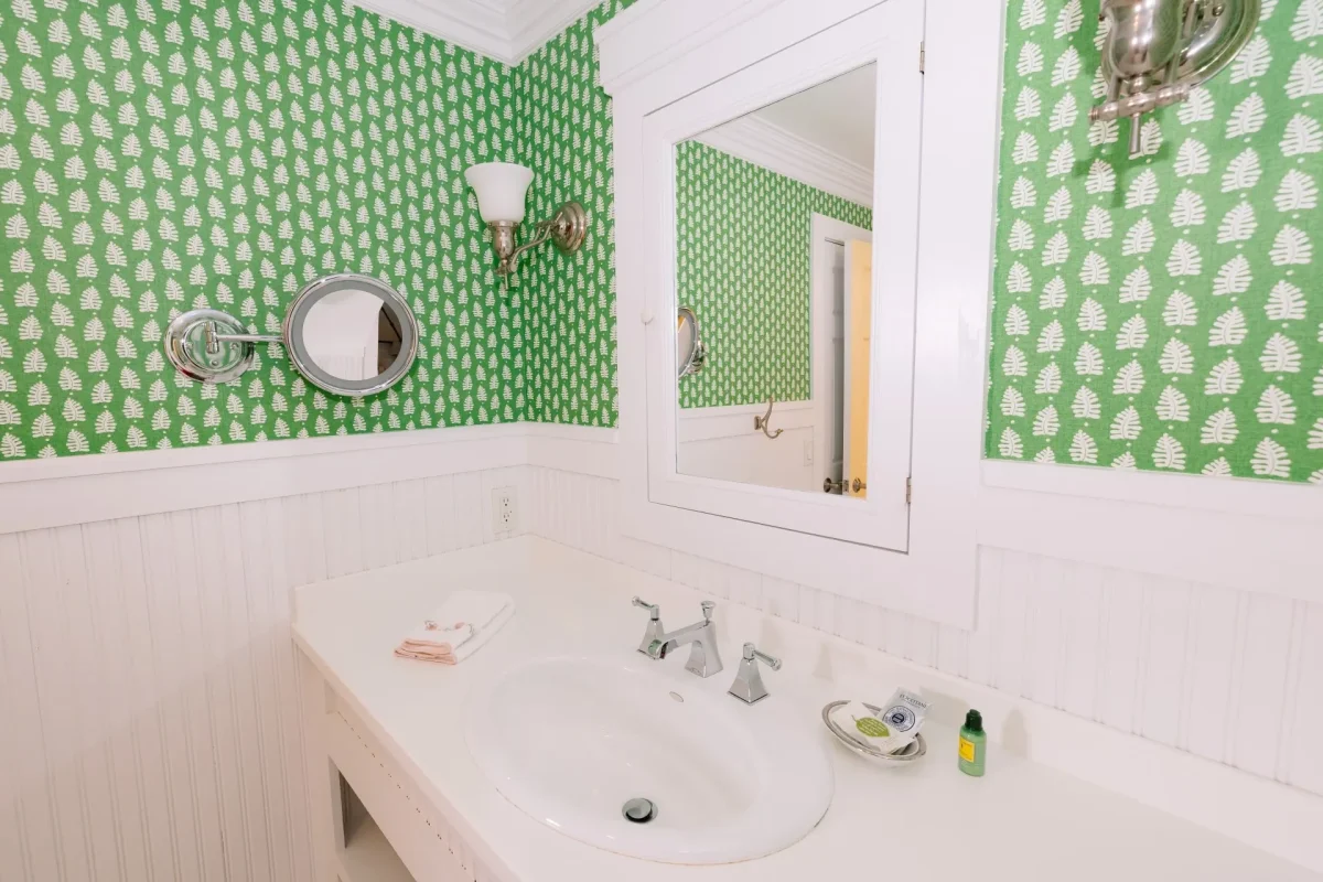 A white bathroom with green accent wallpaper with view of the sink and mirror.