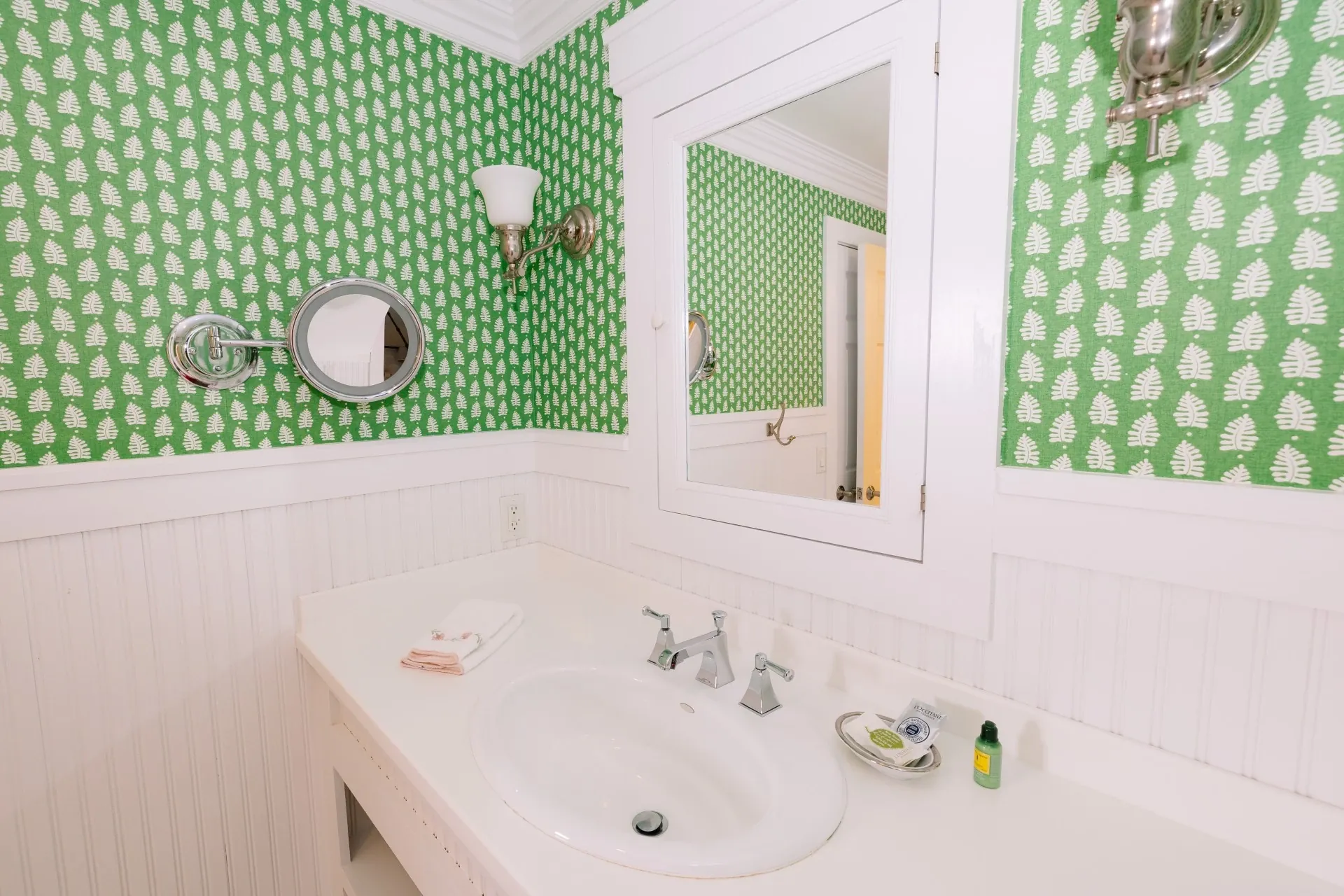A white bathroom with green accent wallpaper with view of the sink and mirror.