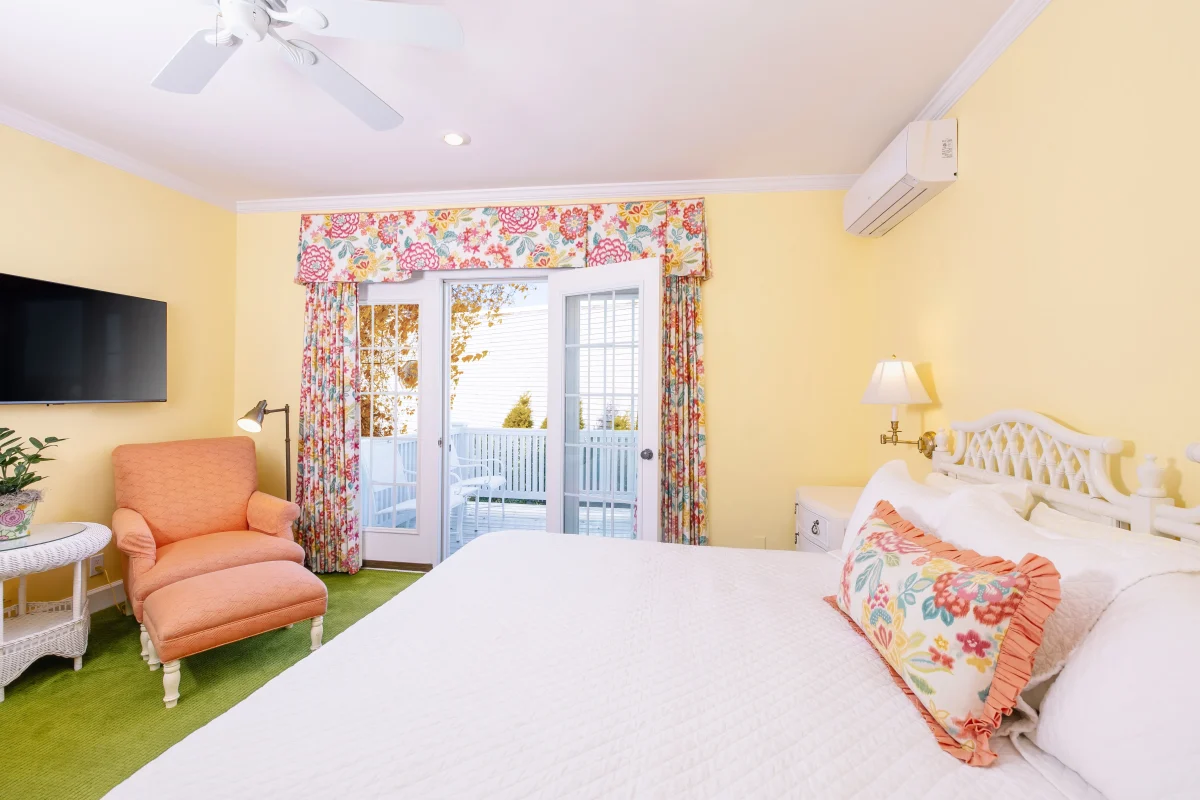 A white bed and an orange room looking onto a balcony with accent curtain.