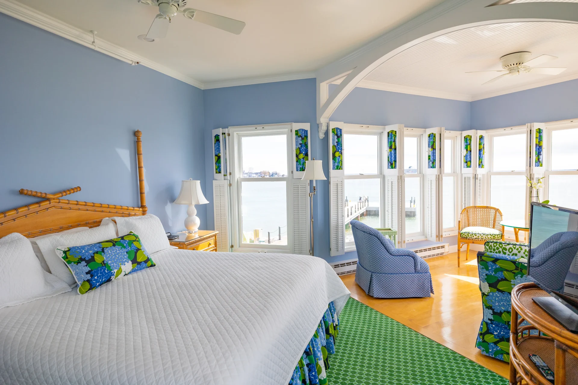 A bed in a blue room with a lot of windows with some blue seats.