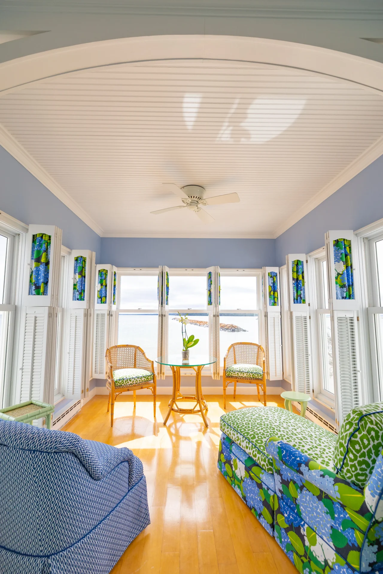Lots of natural light coming in through windows into a blue room with white ceiling. Wood floor with chairs