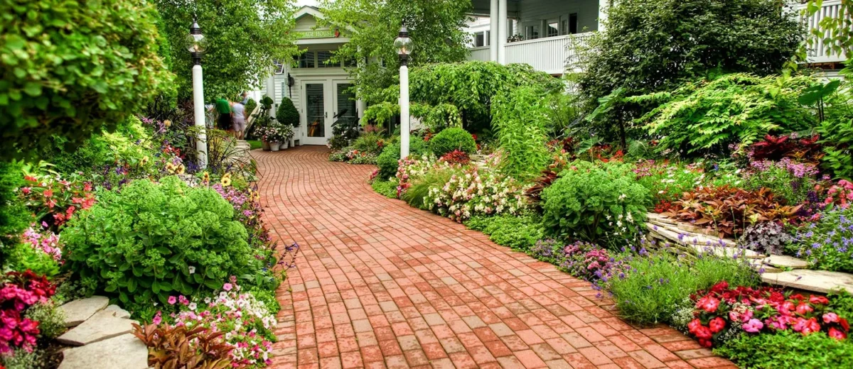 A brick path leading through a beautiful flower and bush garden.