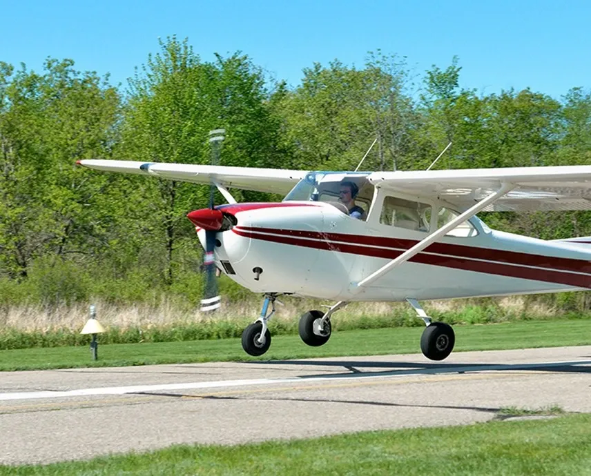 A white plane with red striped single propeller taking off on a landing strip.