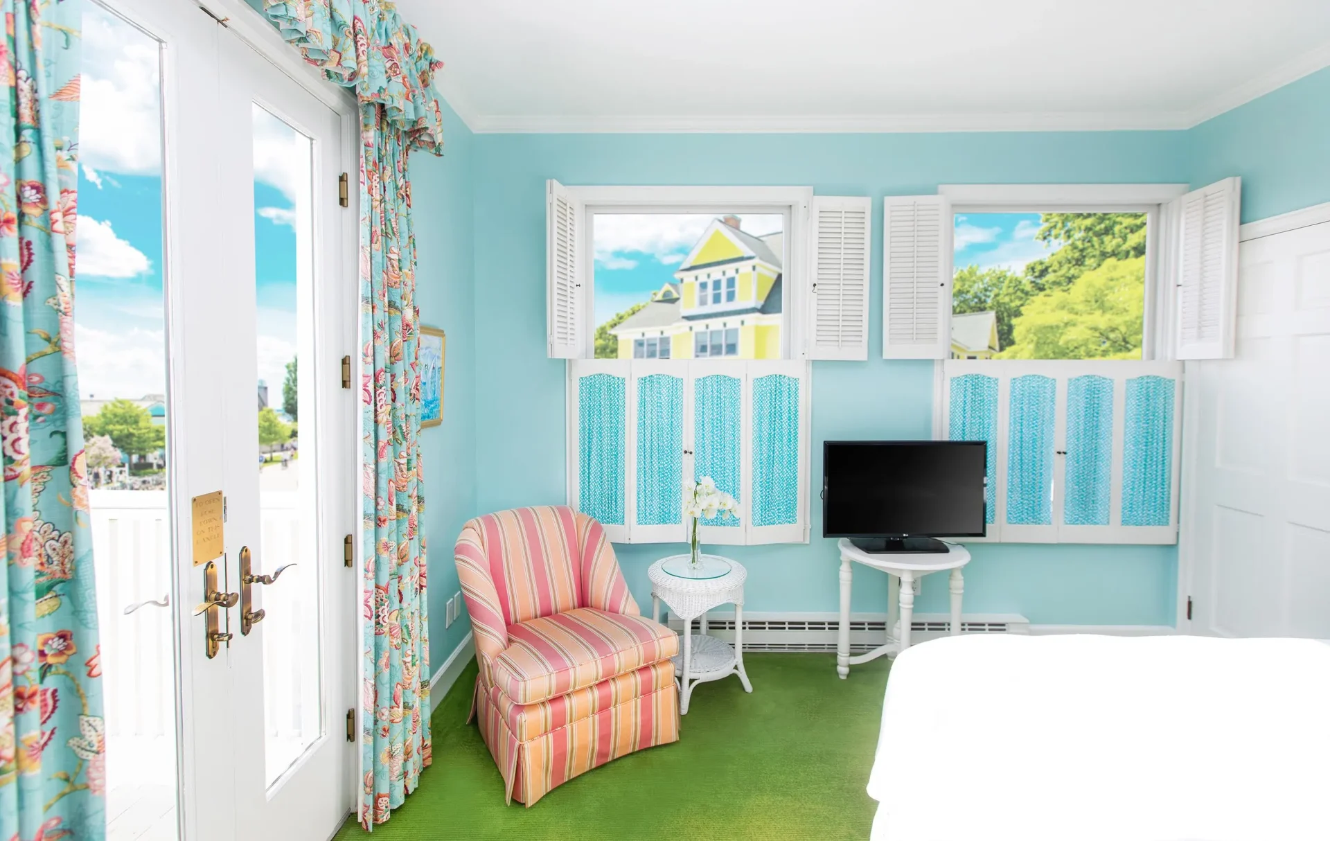 A blue room with a television windows and pink chair.