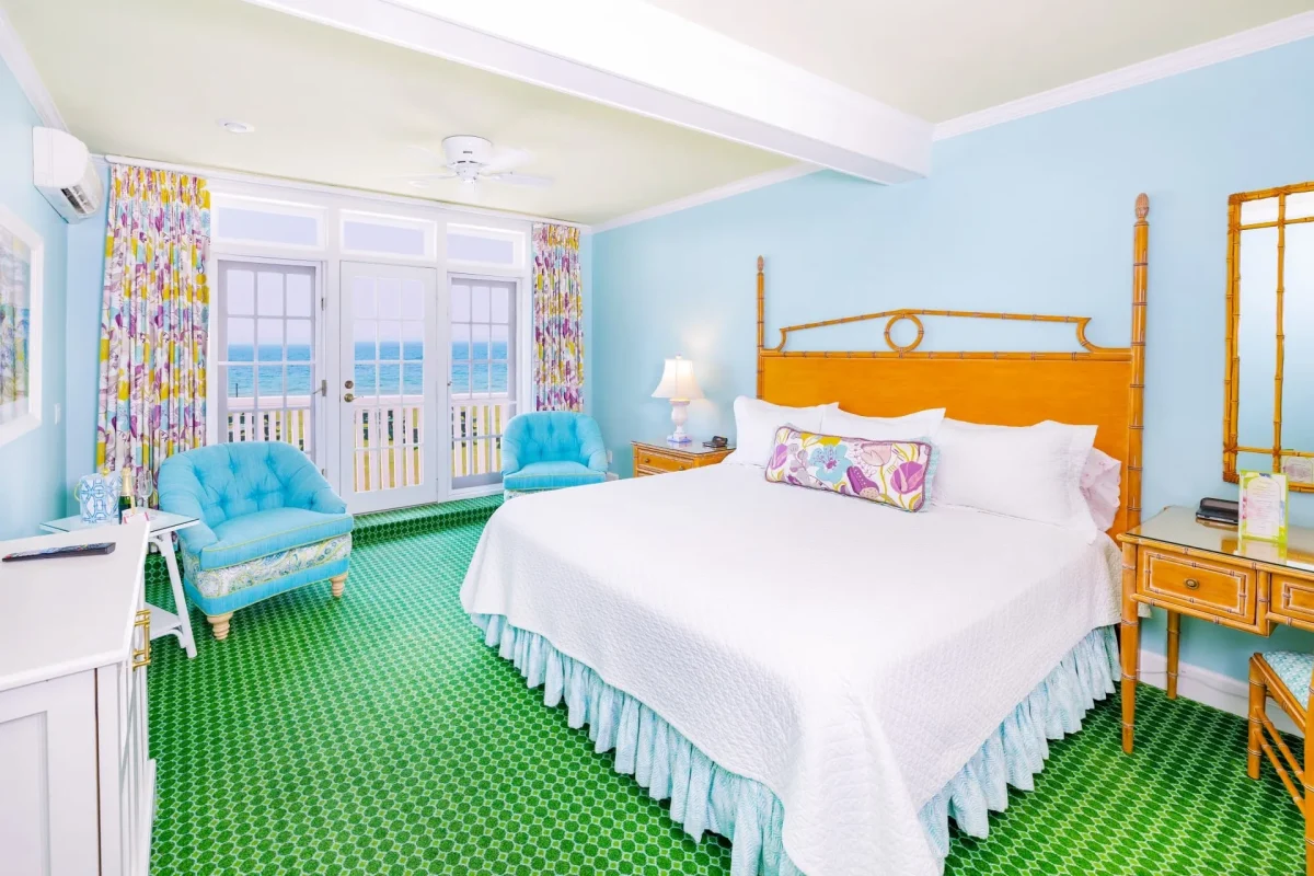 A white bed and a blue room with green carpet looking out to a balcony with doors.