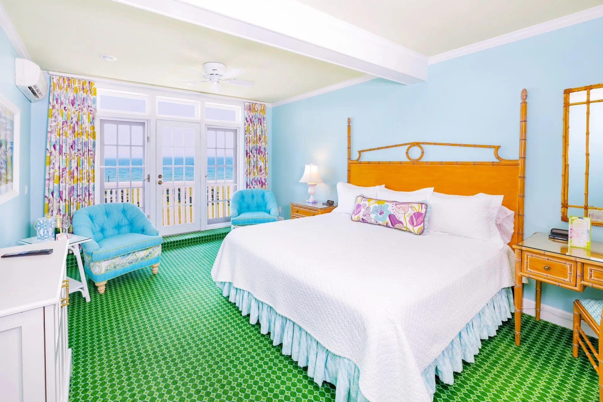 A white bed and a blue room with green carpet looking out to a balcony with doors.