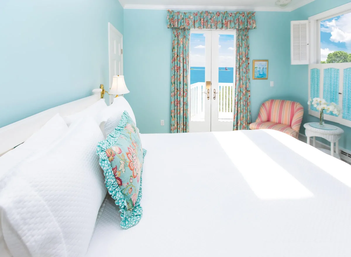 white bed in a blue room with accent pillow, accent curtains with balcony.
