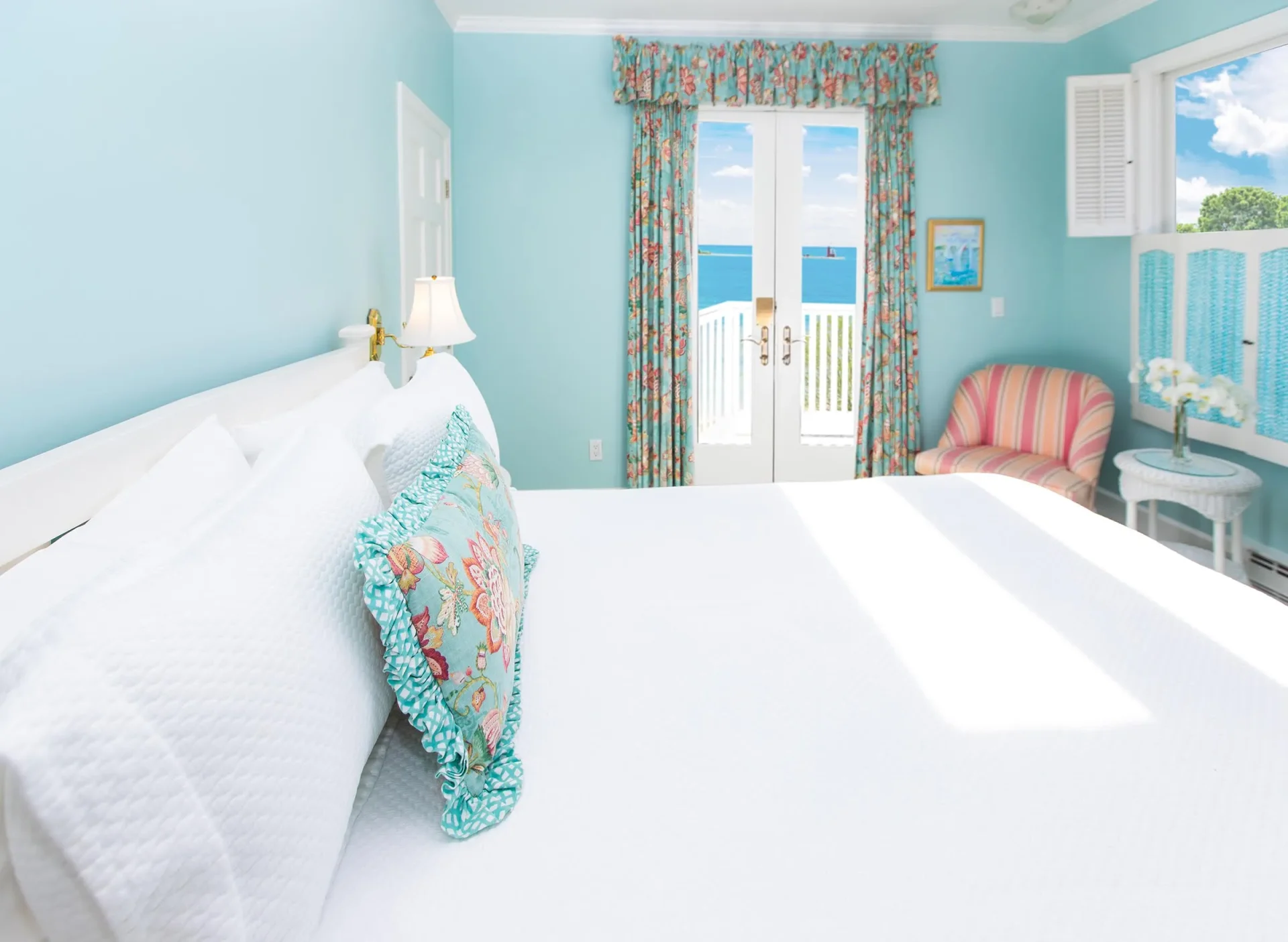 white bed in a blue room with accent pillow, accent curtains with balcony.